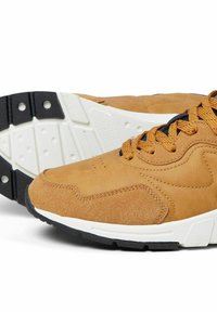 Sneaker in suede tan con lacci neri. Presenta una robusta intersuola bianca e una suola in gomma nera testurizzata. Forma arrotondata con dettagli di cucitura sottili.