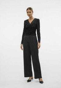 Haut en dentelle noire avec des détails froncés, décolleté en V et manches longues, assorti à un pantalon large à rayures noires et à des escarpins noirs à bout pointu.
