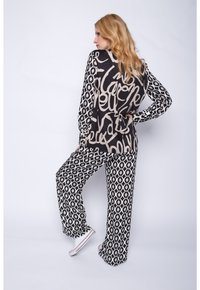 Schwarz-weiß gemustertes Outfit mit einem lockeren Oberteil mit abstrakten Schriftzügen und weitem Bein-Hosen mit geometrischen Formen.