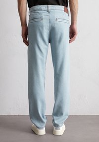 Jasnoniebieskie dżinsy z prostym krojem, posiadające dwie tylne kieszenie oraz brązową skórzaną naszywkę na pasie, noszone z białymi trampkami.