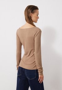 Beige gerippter Langarm-Top mit weitem Ausschnitt, figurbetonter Silhouette, strukturiertem Stoff und schmal zulaufenden Ärmeln, kombiniert mit dunklen Jeans.