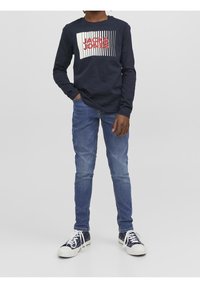 Marinblå långärmad t-shirt med ett vitt och rött grafiskt tryck, i kombination med ljusblå denimjeans och svarta sneakers med vita sulor.