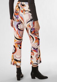 Kleurrijke flared broeken in een draaierig abstract patroon, met tinten oranje, paars en zwart, en een zachte stoftextuur. Zwarte enkellaarsjes.