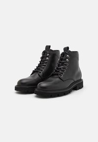 Bottines en cuir noir avec une finition lisse, bouts ronds, quincaillerie argentée et semelle dentelée noire pour la traction. Comprend un design à lacets.