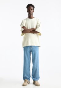 Camisa amarilla claro de manga corta y oversize combinada con jeans de mezclilla azul holgados y zapatillas beige con acentos oscuros.