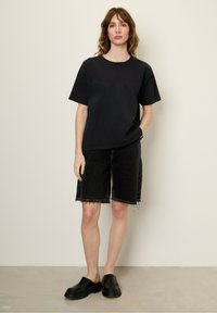 Melna kokvilnas T-kreklu ar īsām piedurknēm, apvienots ar melniem džinsa šortiem ar saplēstiem malām. Valkāts ar melniem slip-on apaviem. Vienkāršs dizains.