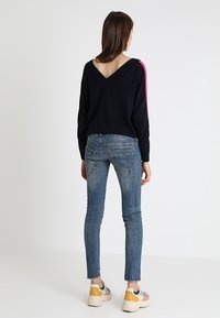 Mörkblå tröja med V-ringning och rosa detaljer längs ärmarna, matchad med åtsittande blå jeans och flerfärgade sneakers.