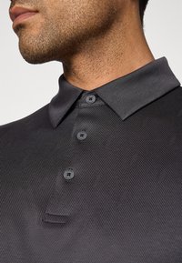 Close-up of a man wearing a dark gray textured polo shirt with three buttons and a pointed collar.