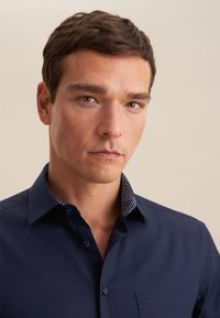 Camicia blu navy con colletto interno a pois in contrasto. Dotata di taschino e texture liscia.