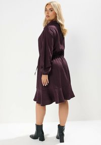 Abito plum con bottoni, texture a coste, vita elastica e orlo svasato, indossato con stivali neri alla caviglia. La vista posteriore mostra maniche lunghe.