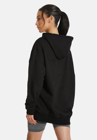 Sudadera negra de gran tamaño con capucha ajustable y puños acanalados, fabricada en tejido suave, presenta un diseño holgado y sin logotipos visibles.