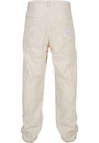Beige bomull cargo bukser med baklommer, sidelommer, slitte detaljer på kanten og snøring ved anklene.