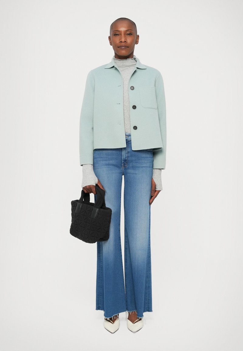 Lichtgroene cropped jack, grijze coltrui, high-waisted flared denim jeans, zwarte gestructureerde handtas en witte pointy-toe hakken.