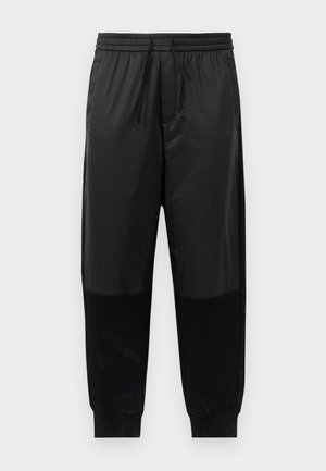 Black athletic pants featuring a blend of smooth and textured fabrics, elastic waistband with drawstring, and tapered cuffs.