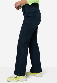 Tmavě modré džíny s rovnou nohavicí, s polovičním pasem, pěti kapsami a jemným prošíváním. V kombinaci s neonovými teniskami.