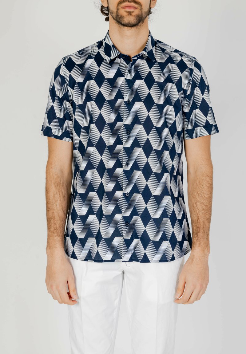 Camicetta a maniche corte con un motivo zigzag geometrico in blu navy e bianco. Presenta una chiusura a bottoni sul davanti e una vestibilità rilassata.