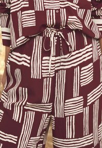 Ensemble en tissu maroon à motifs comprenant de larges rayures blanches disposées de différentes manières. Taille élastique avec une coupe décontractée. Matériau texturé.