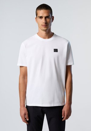 T-shirt bianco in cotone con maniche corte, scollo tondo e un piccolo logo nero applicato sul petto. Texture liscia e design minimalista.
