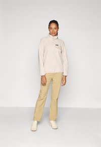 Fleece-Pullover in hellem Beige mit gemusterter Textur und Reißverschlusskragen; kombiniert mit khakifarbenen Hosen und hellen Sneakers.