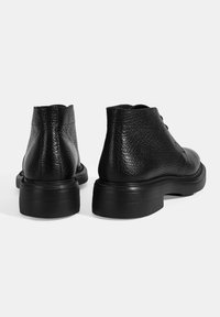 Schwarze Lederstiefel bis zum Knöchel mit strukturierter Oberfläche, runder Zehenform und dickem Gummisohle. Sie verfügen über sichtbare Schnürung und eine kurze Schafthöhe.