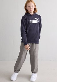 Ναυτικό φούτερ με λευκό λογότυπο "PUMA", γκρι cargo παντελόνια με τσέπες και λευκά αθλητικά παπούτσια με λογότυπο PUMA. Λείος ύφασμα και άνετη εφαρμογή.
