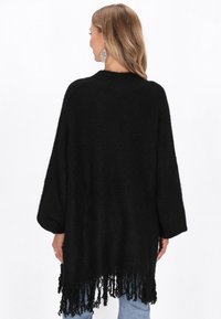 Schwarzer oversize Strickpullover mit weiten Ärmeln und franjierter Saum. Weicher Stoff, einfaches Design und lockere Passform.