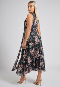 Kukkakuosiset maksimekko tummansinisenä, jossa on vaaleanpunaisia ruusuja. Ominaisuuksiin kuuluu olkaimeton malli ja vyötäröllä solmittava vyö. Virtaava kangas ja nilkkapituiset helmat.