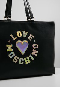 Zwarte handtas van nepleer met de tekst "LOVE MOSCHINO" en een iriserend hartontwerp. Met dubbele handvatten en een rechthoekige vorm.