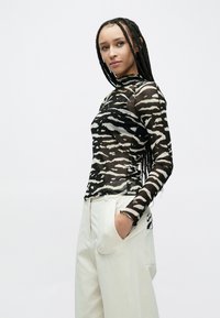 Sort og cremefarvet langærmet mesh-top med tigerstribet mønster, kombineret med lyse, løstsiddende bukser. Tekstureret stof fremhævet.