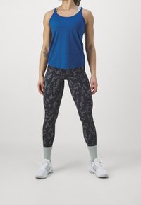Canottiera sportiva blu, leggings neri con motivo e sneakers bianche con dettagli verde menta. Materiali lisci con un design aderente.