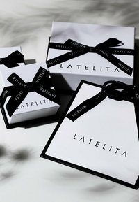 Tre vita presentlådor med svarta snören, försedda med "LATELITA"-logotypen i fet svart text. Den största lådan har en svart kant.