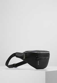 Mustat tekonahkaiset vyölaukut, joissa on sileä pinta, kaareva muotoilu, säädettävä hihna ja vetskareilla varustettu etutasku, joka sisältää koristeellista metalliosaa.