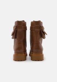 Stivali alla caviglia in pelle marrone con punta arrotondata, finitura testurizzata, cinturino regolabile con fibbia dorata e suola in gomma robusta.