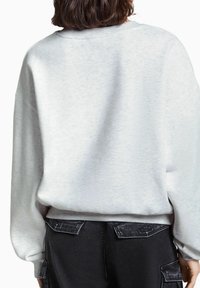 Vaaleanharmaa collegepaita, jossa on pehmeä tekstuuri, pyöreä pääntie ja hieman ylämitoitettu istuvuus. Näkyvät saumat ja resoriset hihansuut. Mustat housut taskuilla.