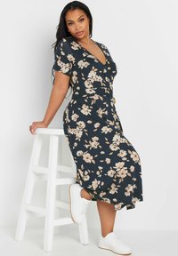 Kukkakuvioinen kynämekko tummansinisellä pohjalla vaaleanpunaisilla kukilla. Lyhyet hihat, V-pääntie, yhätiivistetty vyötärö suurella napilla, yhdistetty valkoisiin tennareihin.