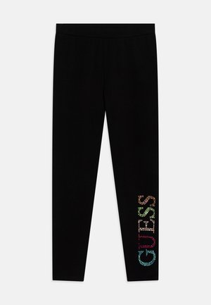 Leggings neri con una texture liscia, dotati di lettering in strass colorati che spellano "GUESS" sulla parte bassa della gamba sinistra.