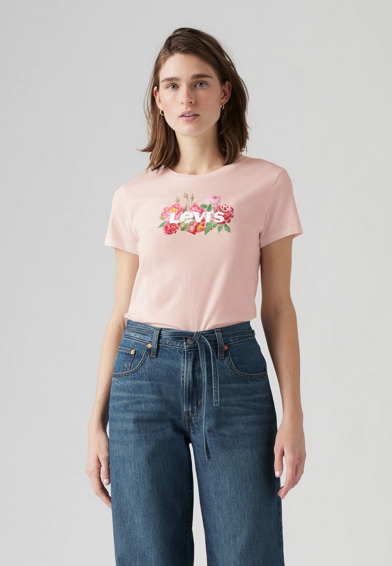 Rosa bomulls t-shirt med blommönster och texten "Levi's", matchad med blå vida denimjeans. Miljön är neutral och ljus.