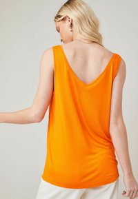 Top arancione senza maniche con design a V sul retro, realizzato in tessuto morbido, caratterizzato da una vestibilità rilassata e una texture liscia.
