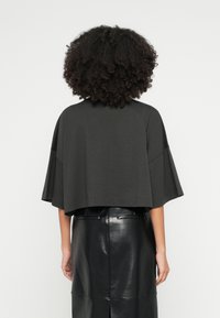 Krátký, tmavě šedý top se širokými, krátkými rukávy. Vyrobený z měkkého materiálu, s jednoduchým designem a rovnou lemem, ve spojení s černou koženou sukní.