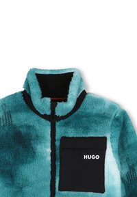 Ζακέτα από φλις με βαθμιδωτή τιρκουάζ απόχρωση, ψηλό γιακά, μαύρο φερμουάρ και τσέπη με το λογότυπο "HUGO" σε λευκό.