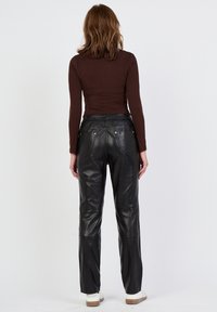 Zwarte leren high-waisted broek met een slim fit, voorzien van achterzakken en minimale stikdetails. Model draagt een fitted bruine top.