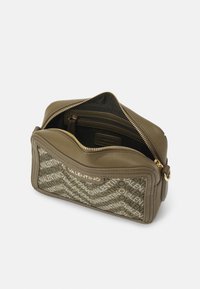 Borsa in pelle verde oliva con chiusura a zip, dotata di un pannello frontale decorato con testo bianco, tasca interna e dettagli in metallo dorato.