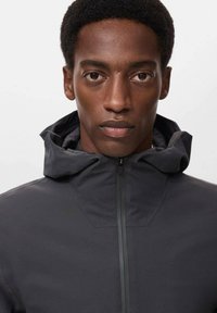 Jacket impermeabilă gri cu guler înalt și glugă, având un fermoar frontal și o textură netedă, mată. Design simplu, modern.