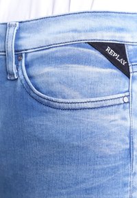 Jeans in denim blu chiaro con un leggero effetto lavaggio. Presentano una tasca frontale e un'etichetta in tessuto nera con la scritta "REPLAY" sulla cintura.