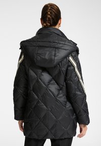 Chaqueta acolchada negra y volumétrica con capucha, que presenta rayas blancas diagonales en las mangas y una textura brillante y suave.
