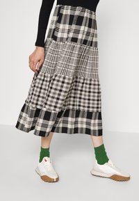 Falda midi a cuadros en blanco y negro con diseño en capas y patrones variados. Combinada con zapatillas blancas y calcetines verdes.