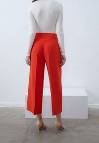 Pantalon large rouge vif en tissu lisse, avec une taille haute et une finition nette, associé à des chaussures à talons hauts couleur nude.