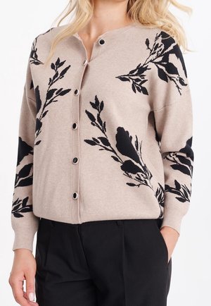 Cardigan beige avec motif floral noir, col rond, boutons à l'avant, manches longues et ourlet côtelé, fabriqué en matière tricot douce.