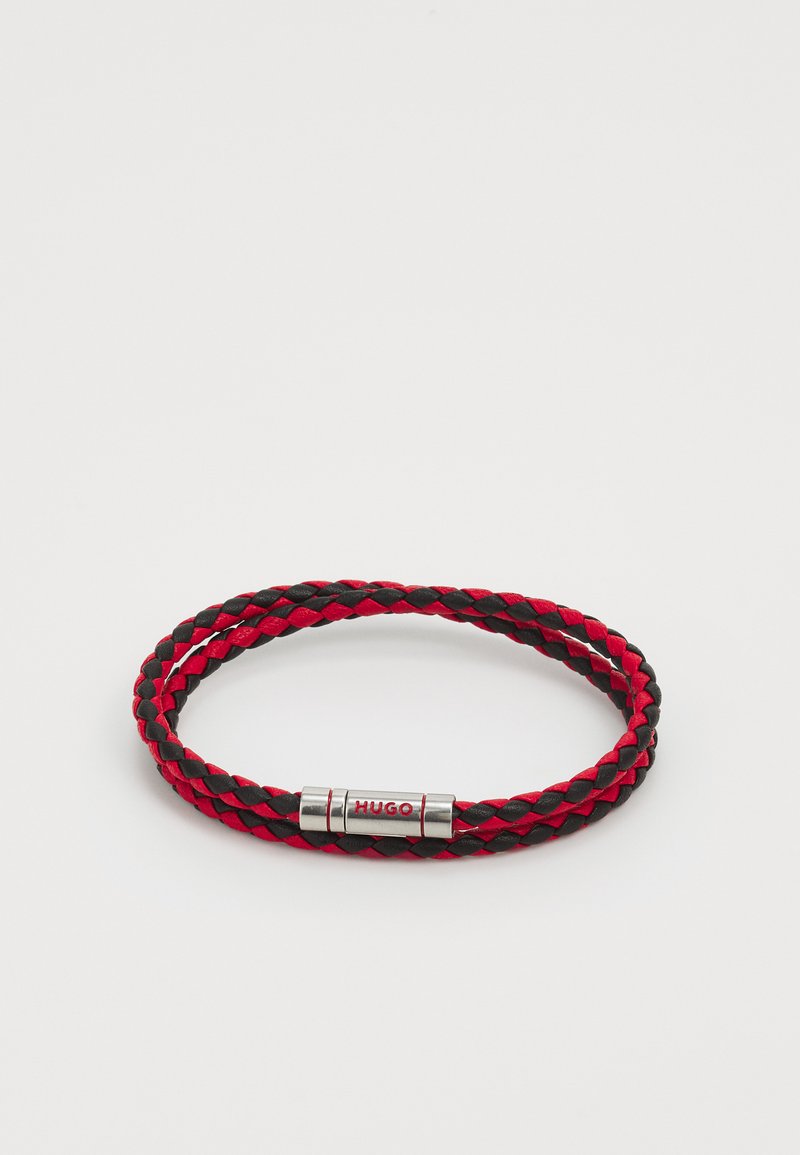 Geflochtenes Armband aus rotem und schwarzem Leder, mit einem silberfarbenen Verschluss, der mit der eingravierten Aufschrift "HUGO" verziert ist. Kompaktes und flexibles Design.