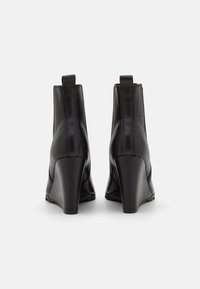 Black leather ankle boots with a pointed toe and wedge heel. Smooth texture, minimal stitching, and rear pull tab for easy wear.